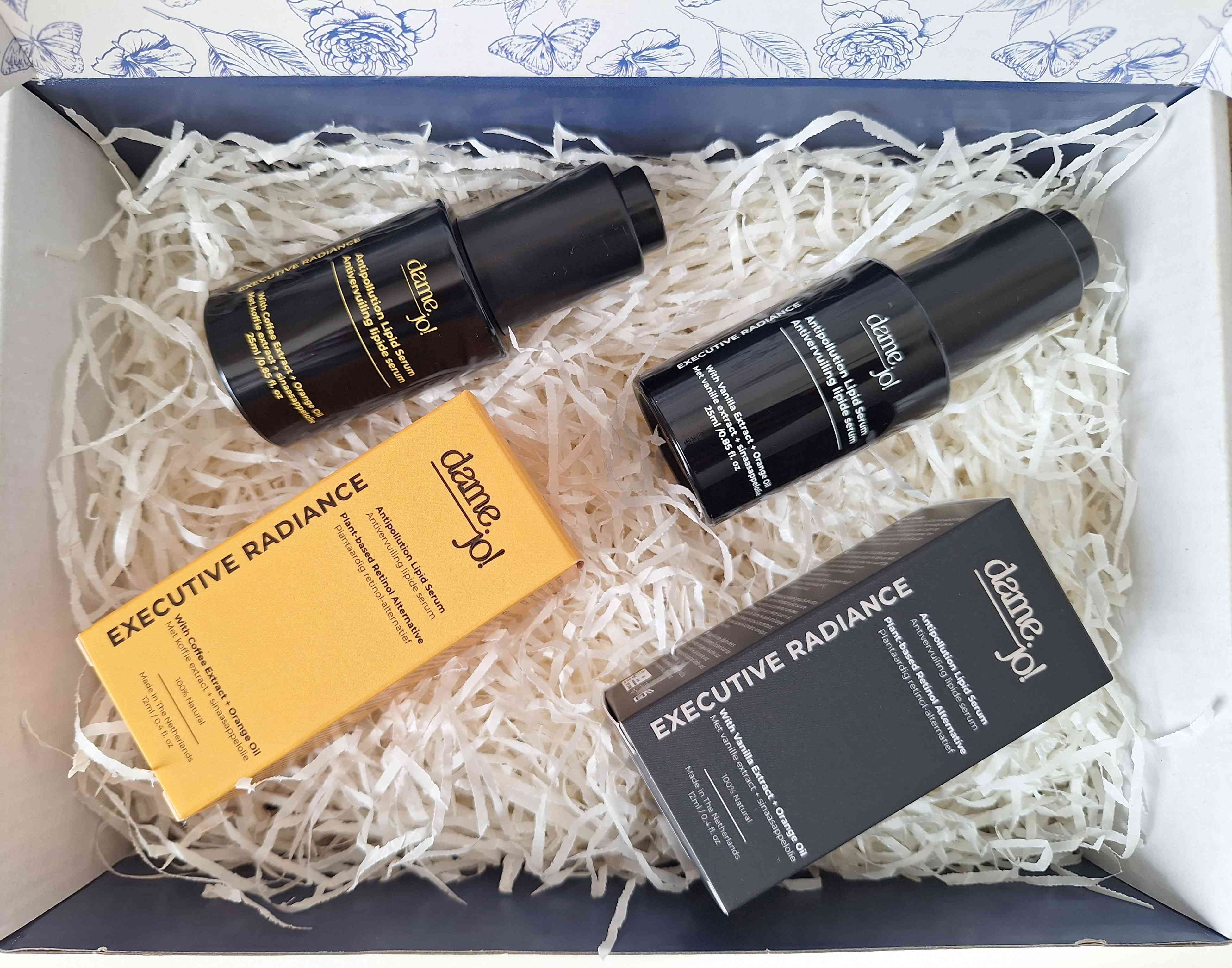Dame Jo! products including bottles and packaging labeled 'Executive Radiance' in a box with shredded paper.