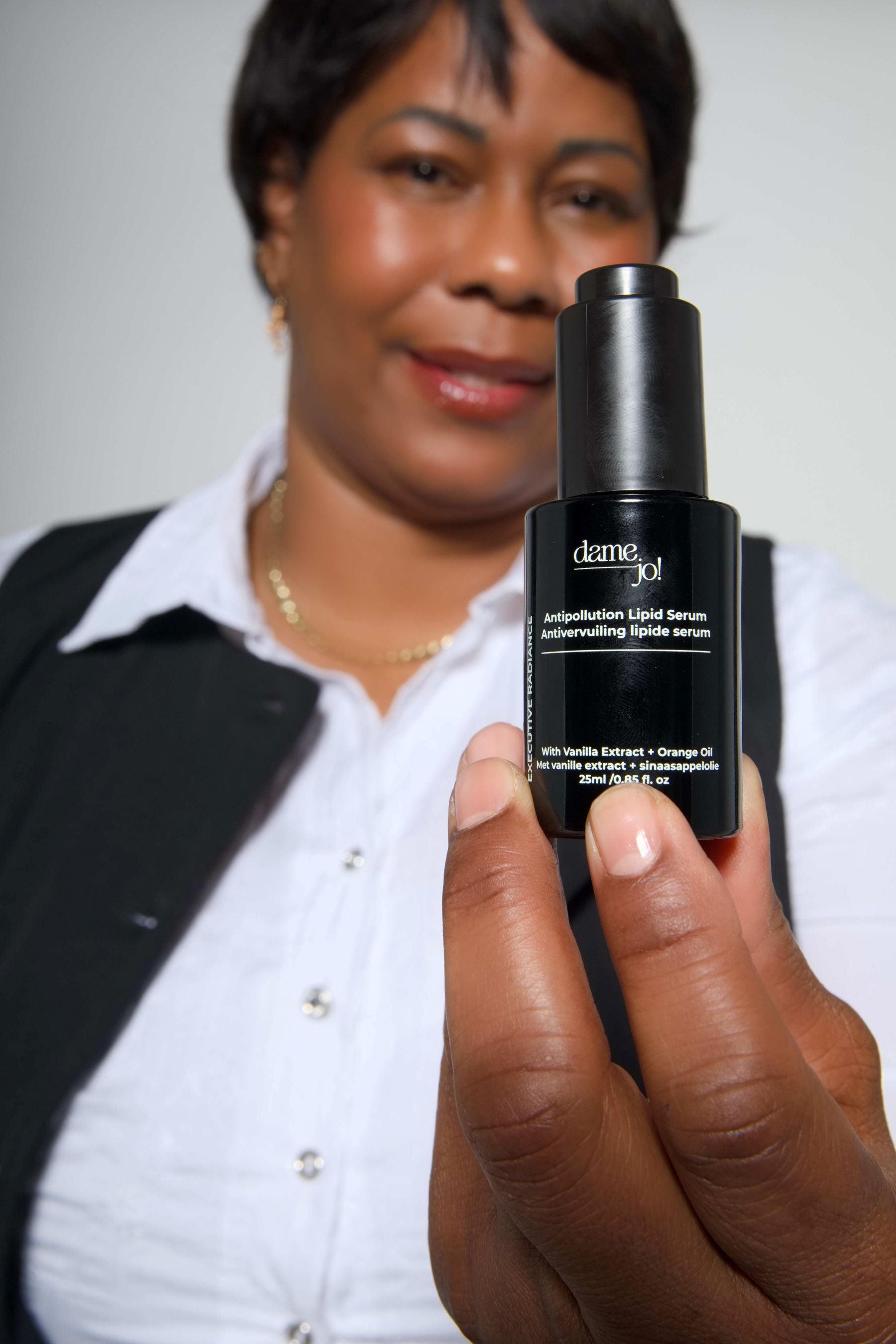 Model holding Dame Jo! serum bottle in front of her, highlighting product packaging.